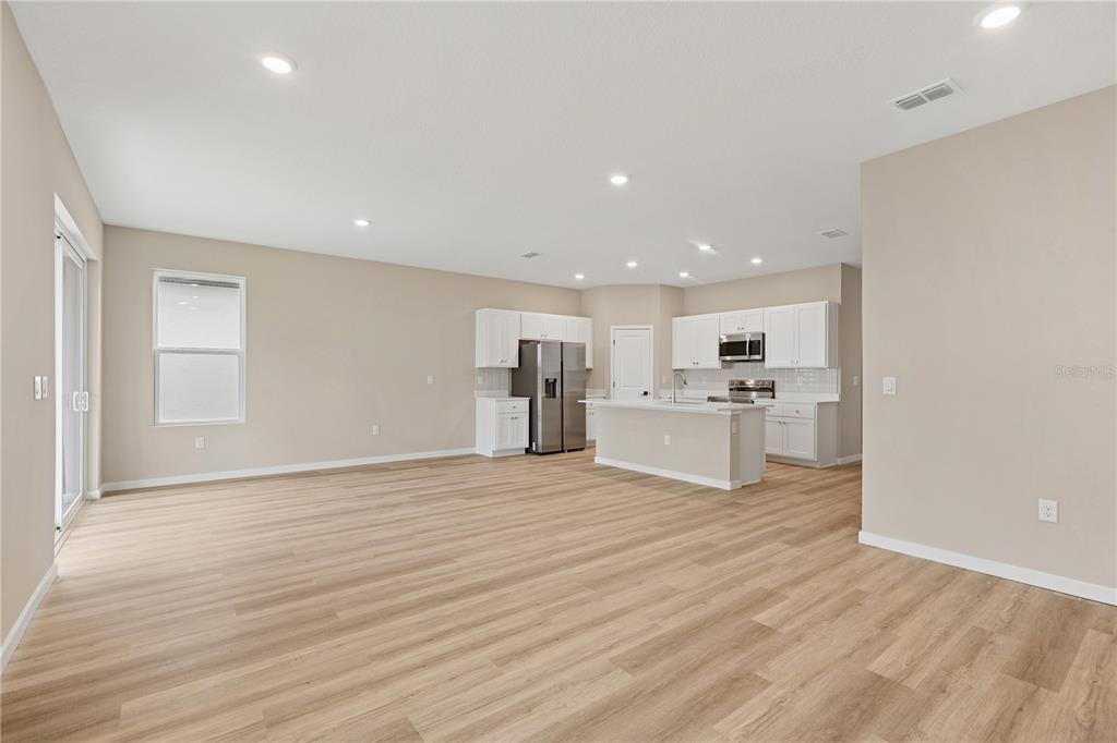 A bright, open-concept kitchen and living area featuring light wood flooring and white cabinetry — 4441 NW 37TH STREET ROAD, OCALA, FL