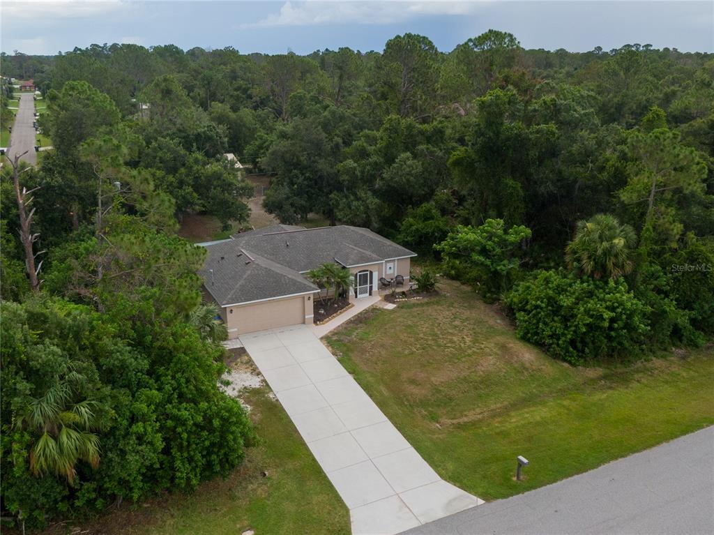 An aerial view shows a single-story house with a concrete driveway surrounded by dense trees — 5175 HORNBUCKLE BOULEVARD, NORTH PORT, FL