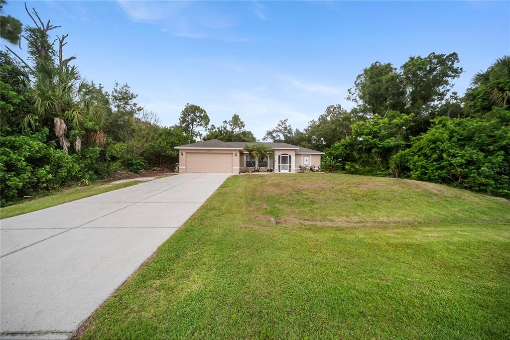 A single-story house with a beige exterior and a concrete driveway sits on a grassy lot — 5175 HORNBUCKLE BOULEVARD, NORTH PORT, FL