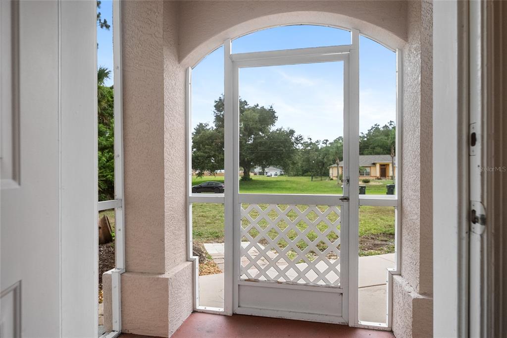 A view from inside a covered porch looking out through a white screen door — 5175 HORNBUCKLE BOULEVARD, NORTH PORT, FL