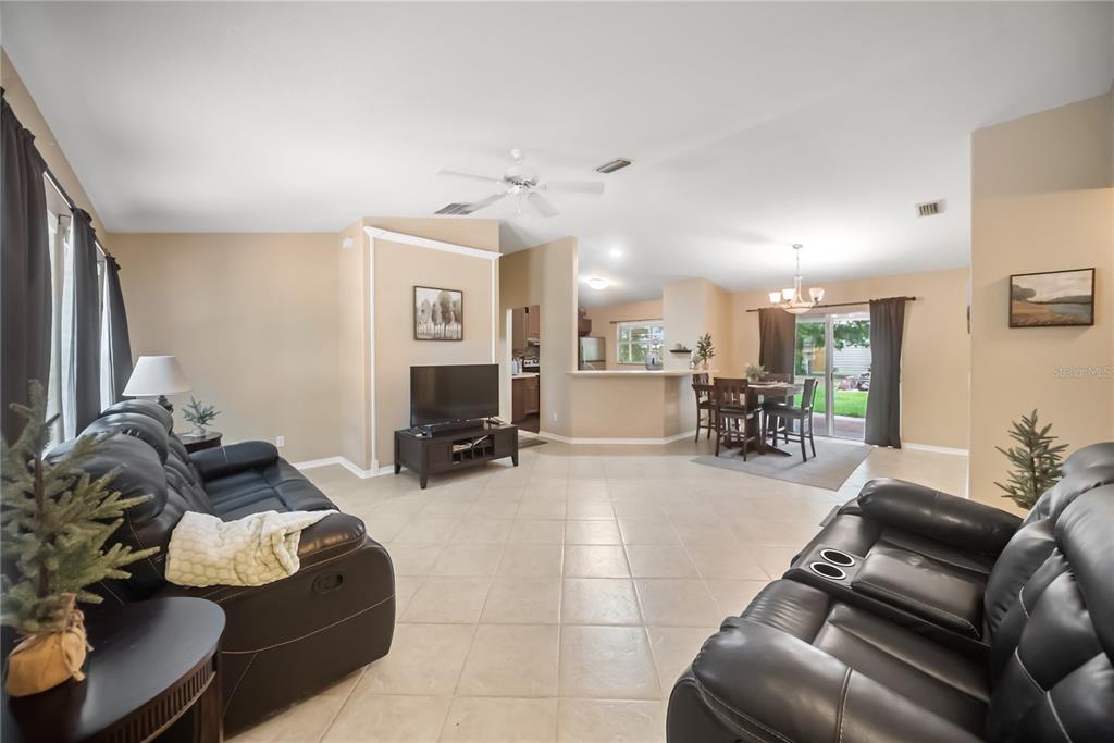 An open-concept living and dining area features tile flooring, black leather furniture, and neutral walls — 5175 HORNBUCKLE BOULEVARD, NORTH PORT, FL