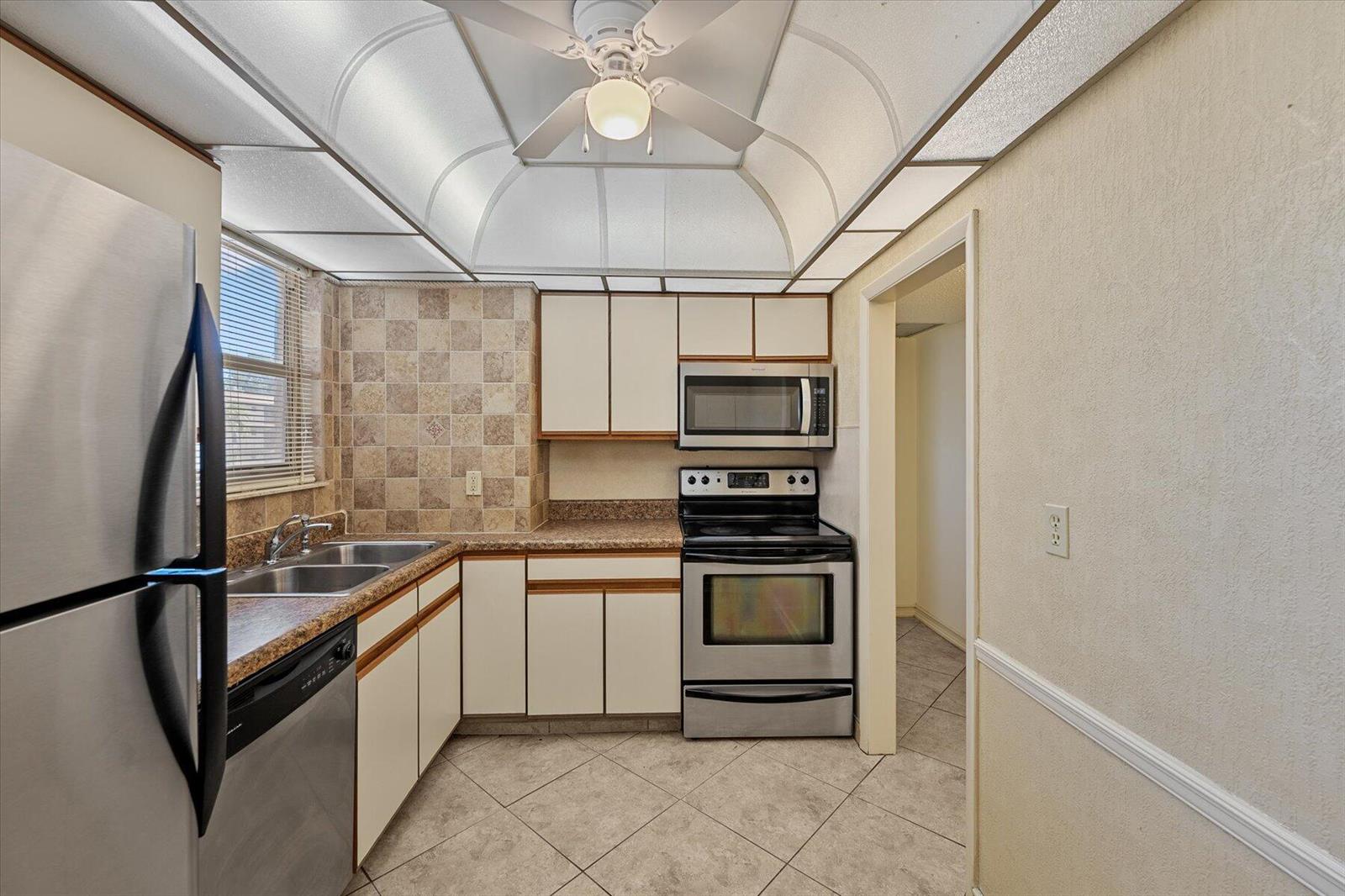A kitchen with stainless steel appliances, white cabinets, tiled backsplash, and a coffered ceiling — 719 Lori Drive # 204, Palm Springs FL 33461, PALM SPRINGS, FL