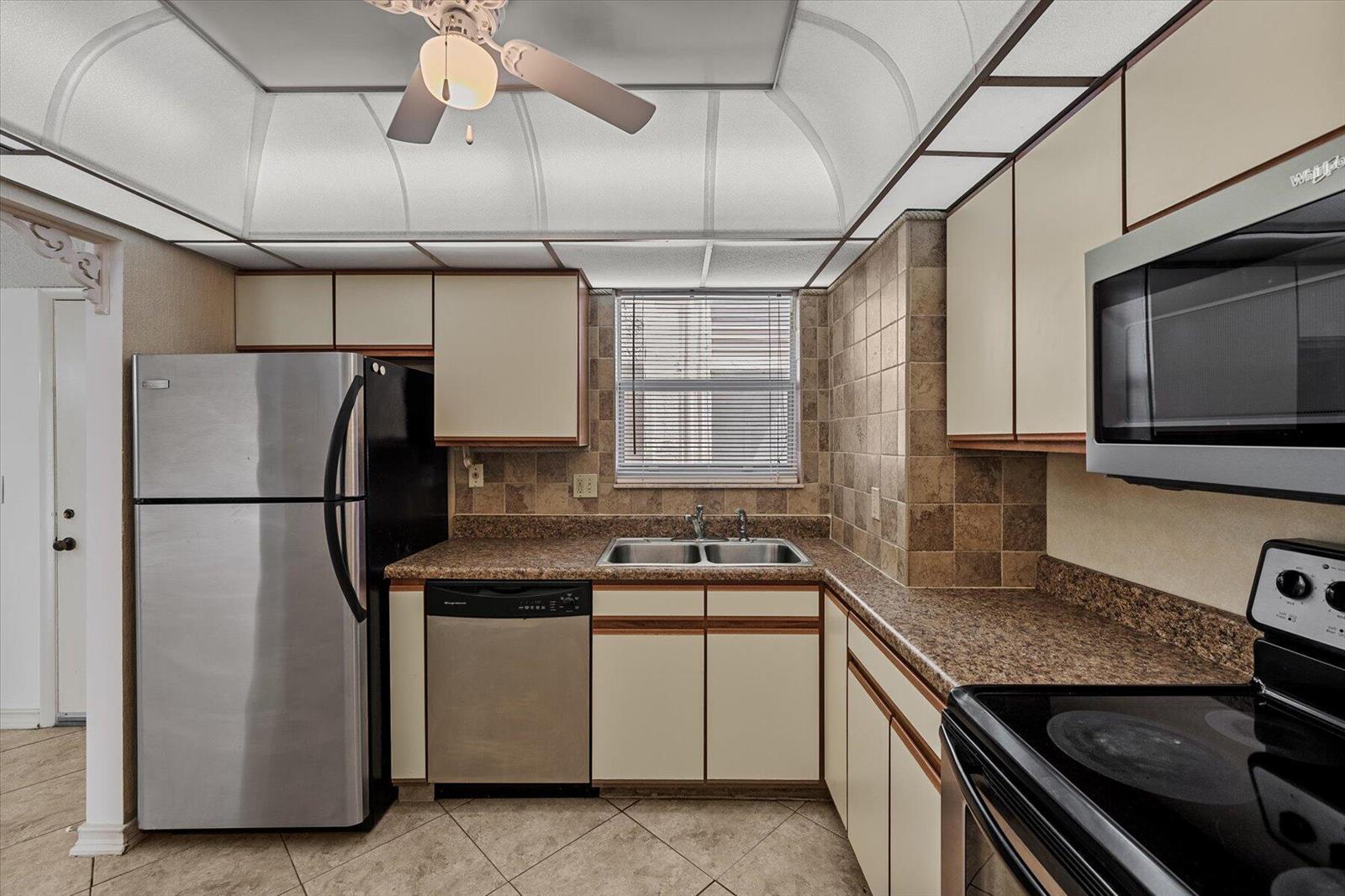 A kitchen features stainless steel appliances, tan cabinets, brown countertops, and a tiled backsplash — 719 Lori Drive # 204, Palm Springs FL 33461, PALM SPRINGS, FL