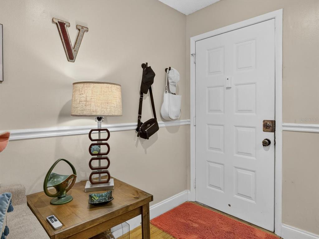 An entryway features a wooden side table with a lamp, wall hooks, and a white door — 6110 CURRY FORD ROAD UNIT 219, ORLANDO, FL