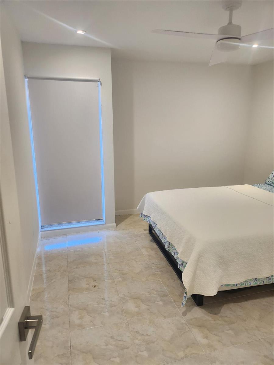 A bedroom with light-colored tile flooring, a white bed, and a window with a blind — 4160 Inverrary Drive # 311, Lauderhill FL 33319, LAUDERHILL, FL