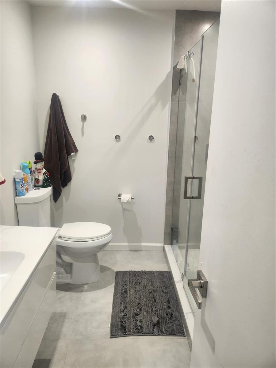A bathroom features a white toilet, a glass-enclosed shower, and a vanity with gray flooring — 4160 Inverrary Drive # 311, Lauderhill FL 33319, LAUDERHILL, FL