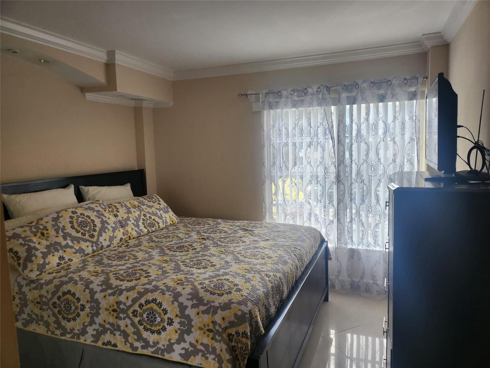 A bedroom features a bed with patterned bedding, a dark wood dresser, and sheer curtains — 4160 Inverrary Drive # 311, Lauderhill FL 33319, LAUDERHILL, FL