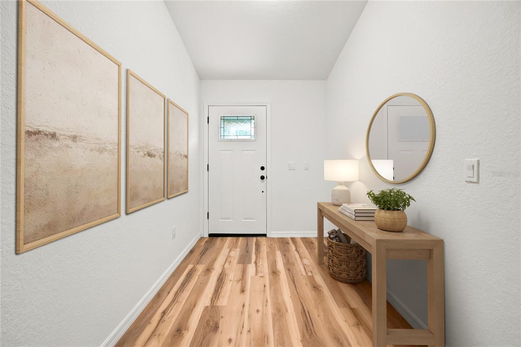 A bright entryway features wood-look flooring, a console table, a round mirror, and wall art — 7784 SW 146TH LANE ROAD, OCALA, FL