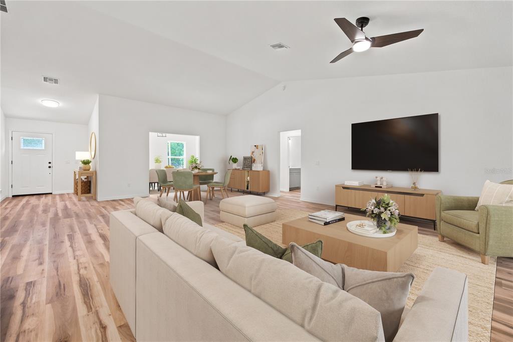 A living room features light wood flooring, a large television, and a neutral-toned sofa — 7784 SW 146TH LANE ROAD, OCALA, FL