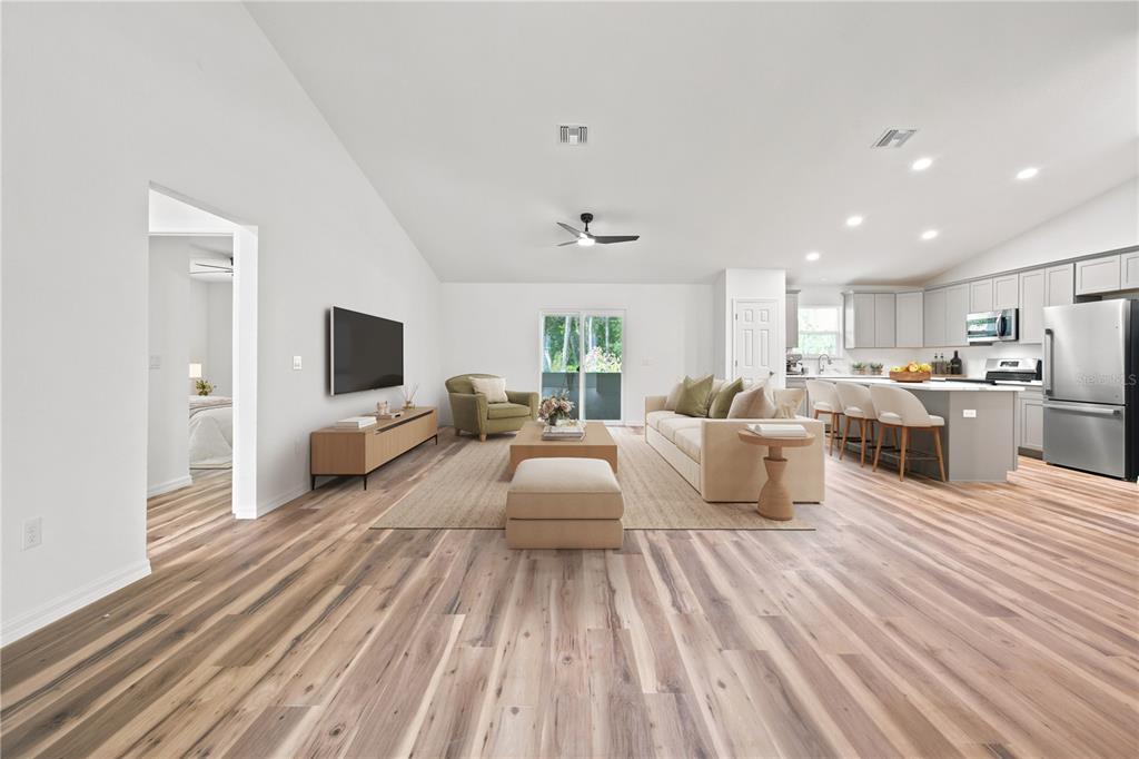 An open-concept living room and kitchen featuring light wood flooring and a vaulted ceiling — 7784 SW 146TH LANE ROAD, OCALA, FL