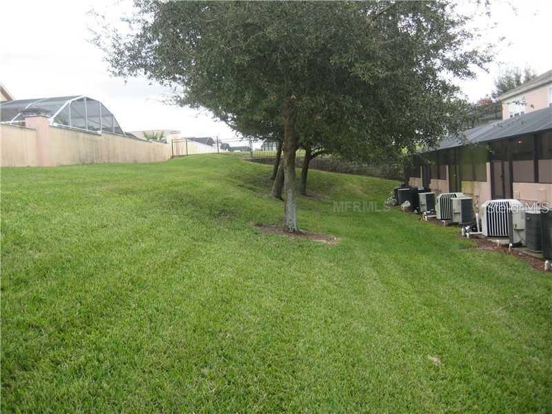 A grassy backyard features a large tree, a privacy wall, and several exterior air conditioning units — 2411 SILVER PALM DRIVE, KISSIMMEE, FL
