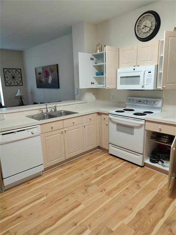 A kitchen features light wood cabinets, white appliances, and a double sink with wood flooring — 2411 SILVER PALM DRIVE, KISSIMMEE, FL
