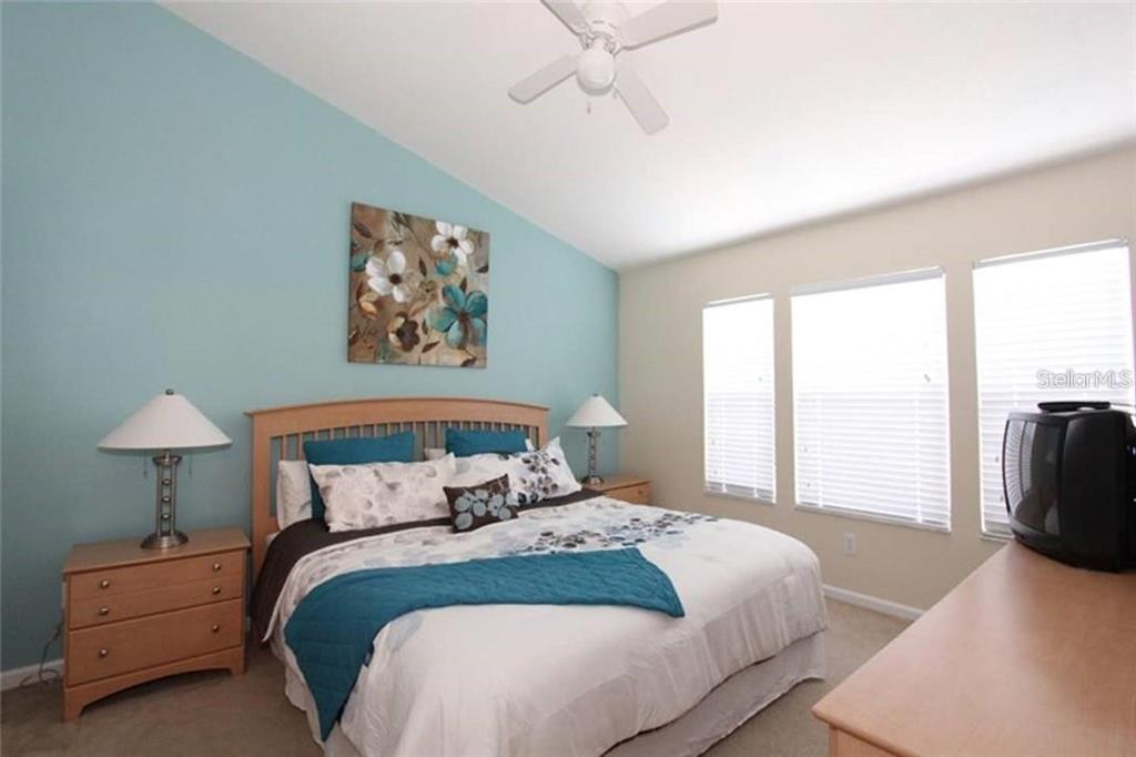 A bedroom features a light blue accent wall, a wooden bed frame, and two windows — 2411 SILVER PALM DRIVE, KISSIMMEE, FL