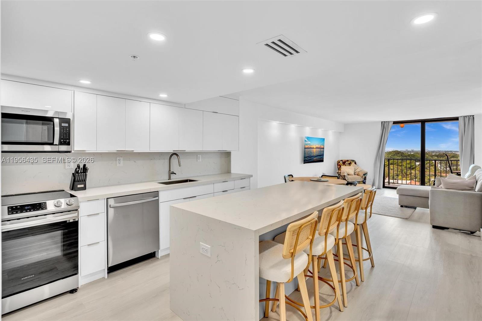 A modern kitchen with white cabinetry and a quartz island opens to a living area — 2625 Collins Ave # 1109, Miami Beach FL 33140, MIAMI BEACH, FL