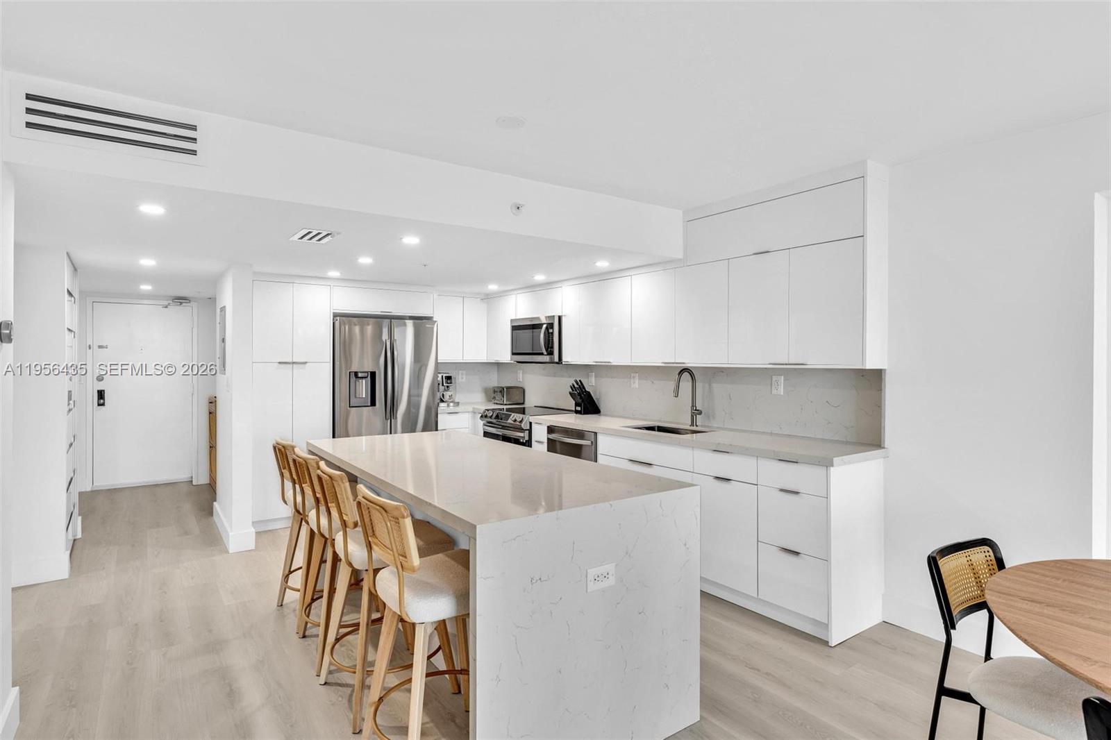 A modern kitchen features white cabinetry, a large quartz island, and light wood flooring — 2625 Collins Ave # 1109, Miami Beach FL 33140, MIAMI BEACH, FL