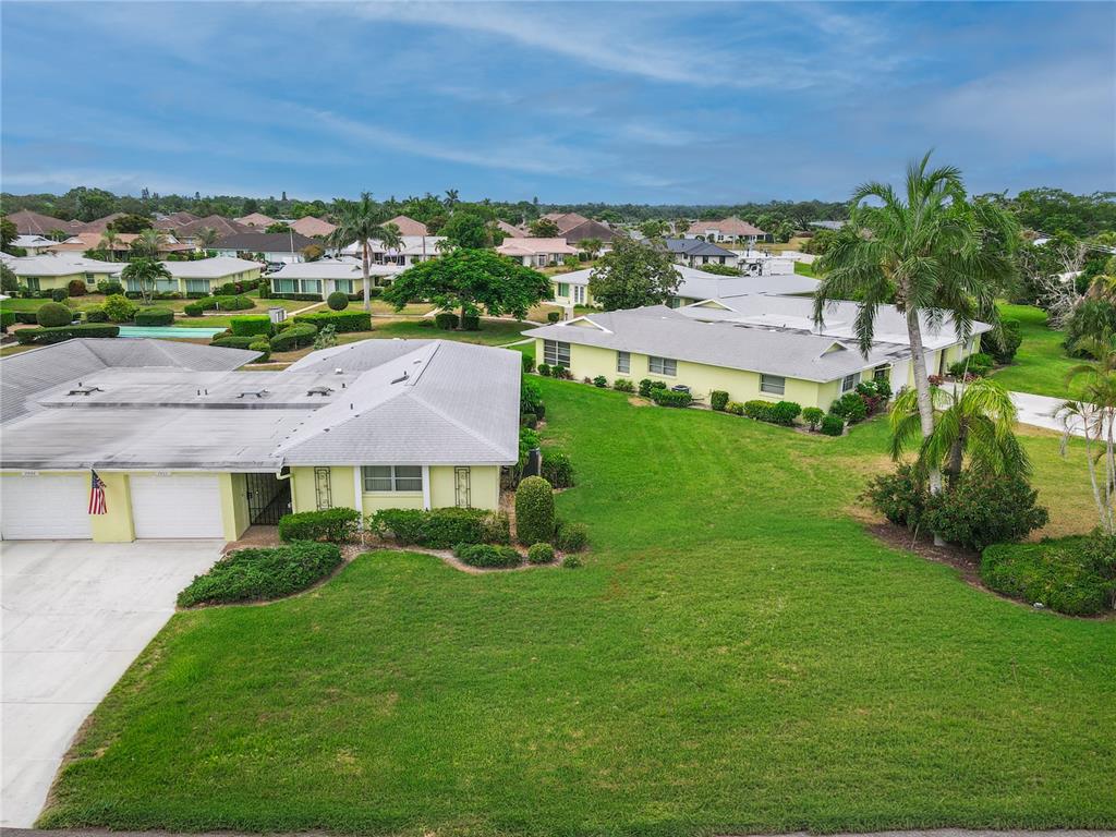 An aerial view shows two light-yellow residential buildings surrounded by green lawns and palm trees — 7011 10TH AVENUE W, BRADENTON, FL