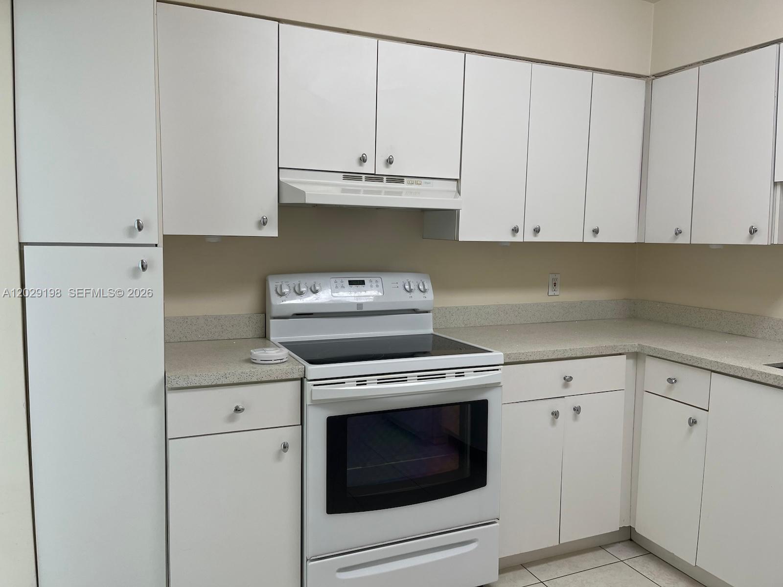 A kitchen features white cabinets, a white electric stove, and speckled light-colored countertops — 5161 Collins Ave # 909, Miami Beach FL 33140, MIAMI BEACH, FL