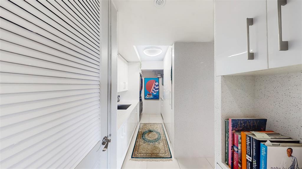 A narrow, white-toned kitchen features a patterned rug, sleek cabinetry, and a framed sailboat print — 00690 COND TREASURE POINT UNIT 372, VEGA ALTA, PR