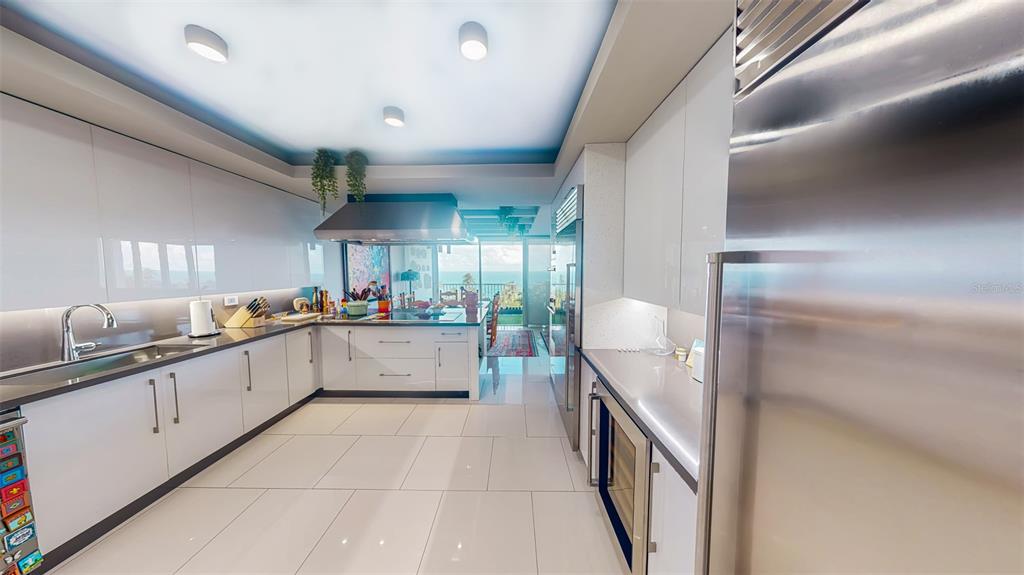 A modern kitchen features white glossy cabinets, stainless steel appliances, and a view of the ocean — 00690 COND TREASURE POINT UNIT 372, VEGA ALTA, PR