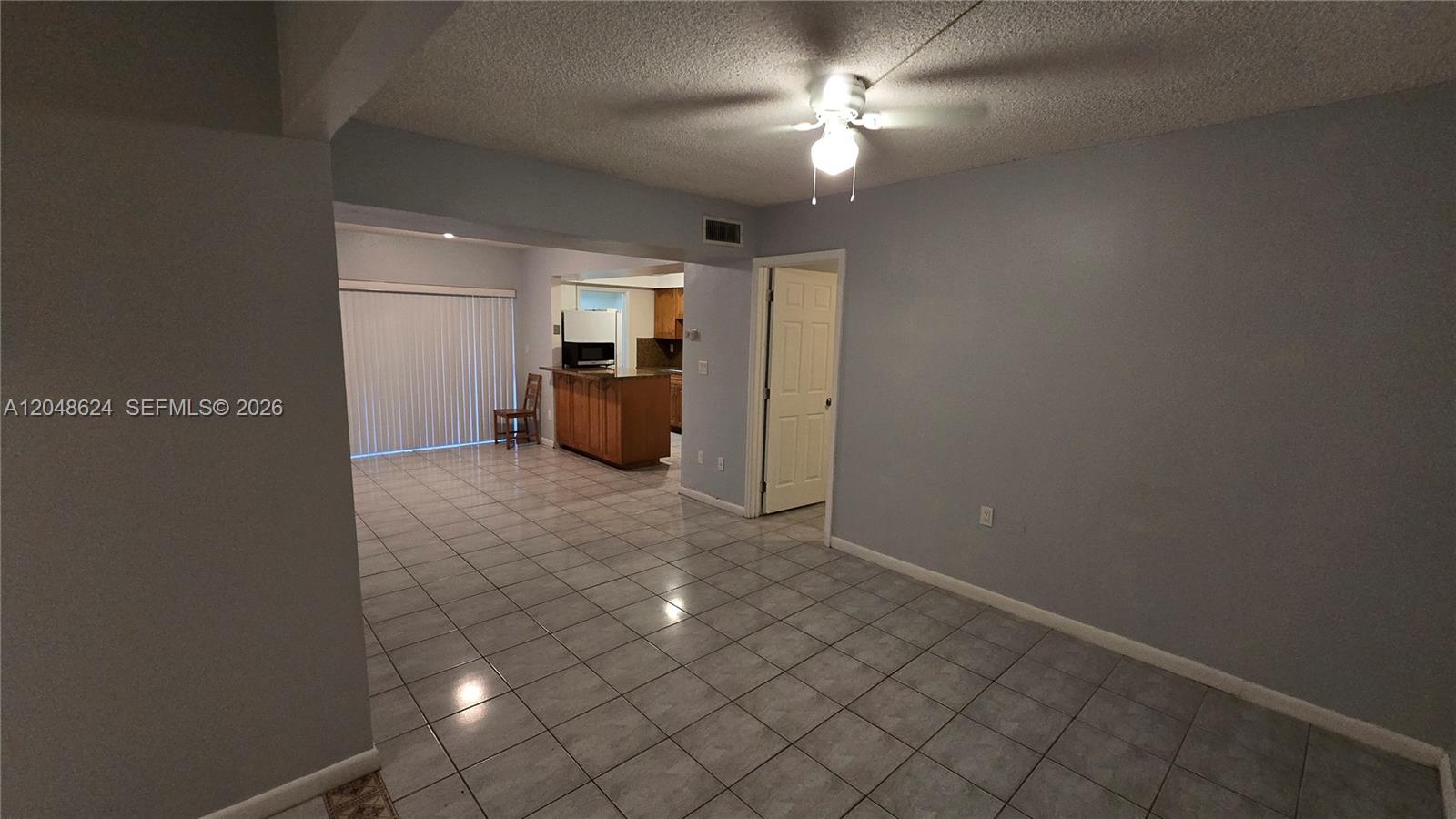 A room with light gray walls and tiled flooring leads to an open kitchen area — 8401 SW 107th Ave # 174E, Miami FL 33173, MIAMI, FL