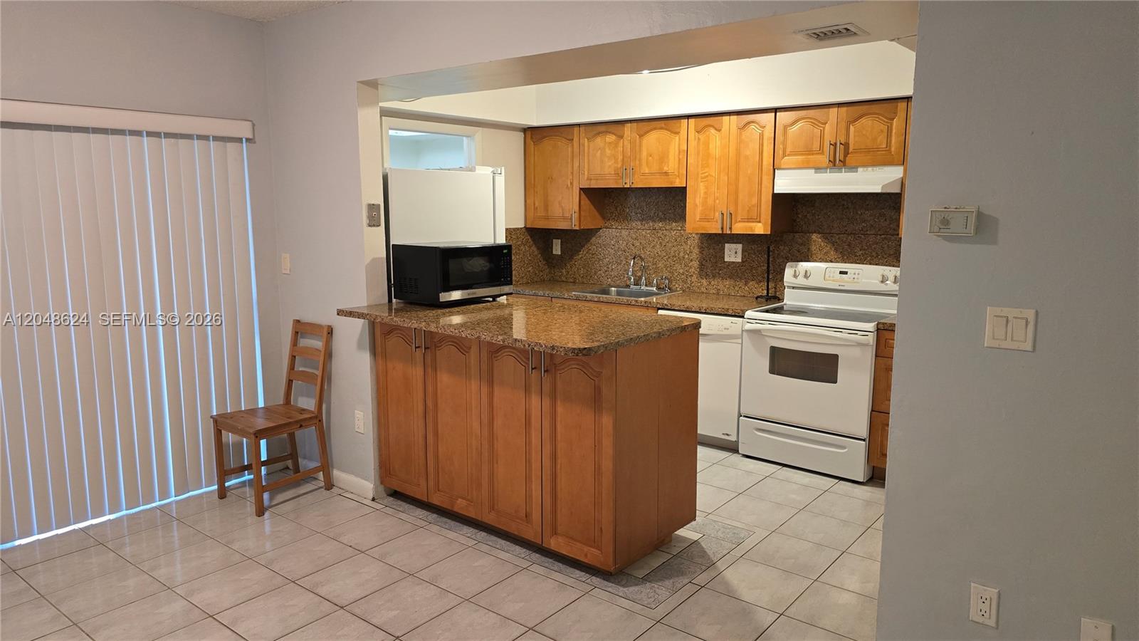 A kitchen features wood cabinets, granite countertops, white appliances, and light-colored tile flooring — 8401 SW 107th Ave # 174E, Miami FL 33173, MIAMI, FL
