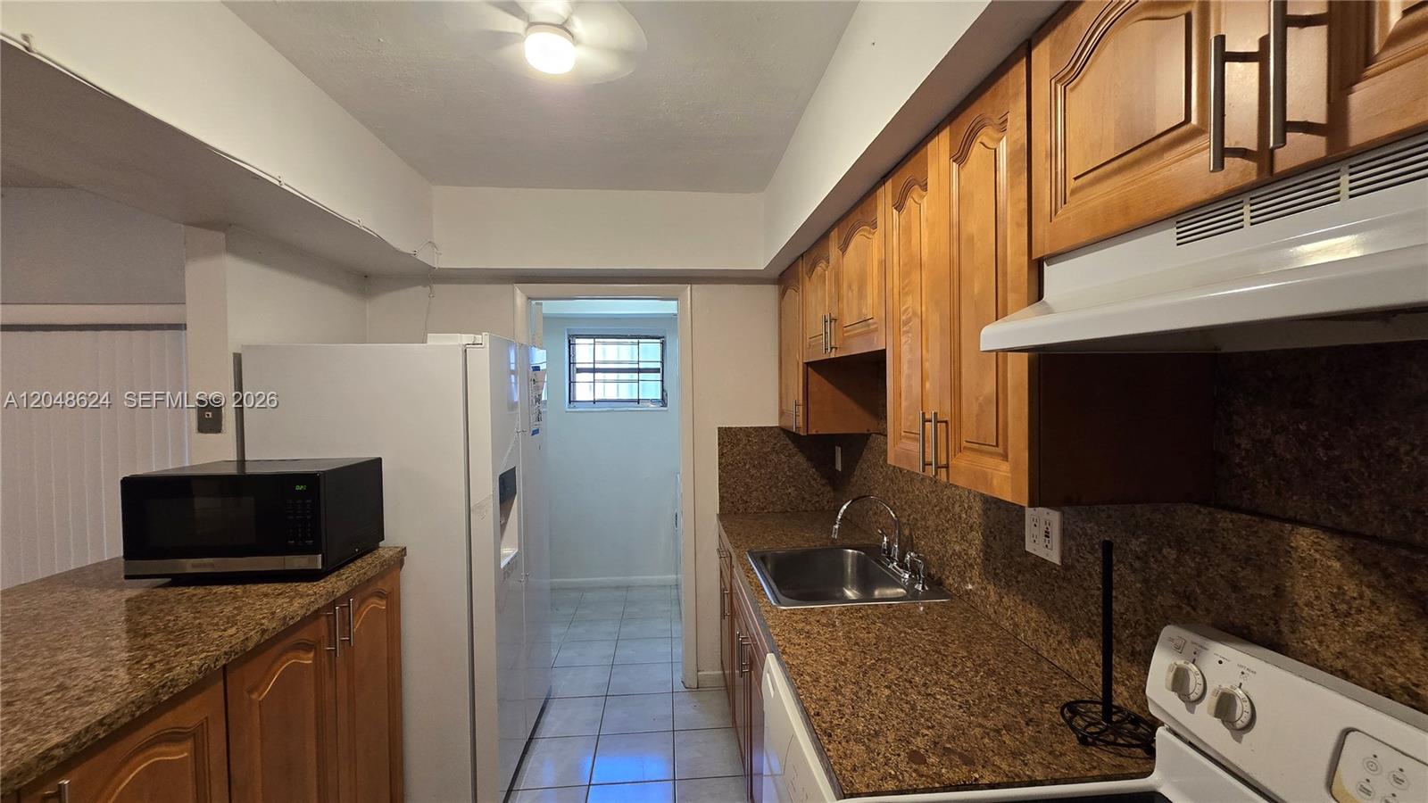 A kitchen features wood cabinets, granite countertops, a stainless steel sink, and white appliances — 8401 SW 107th Ave # 174E, Miami FL 33173, MIAMI, FL