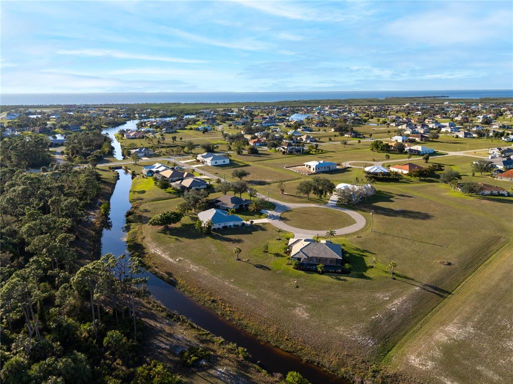 An aerial view shows a residential neighborhood with houses, a canal, and surrounding vegetation — 24351 PENHOLLOW COURT, PUNTA GORDA, FL