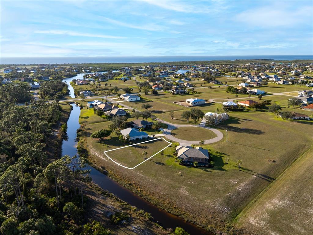 An aerial view shows a vacant residential lot outlined in white next to a canal — 24351 PENHOLLOW COURT, PUNTA GORDA, FL