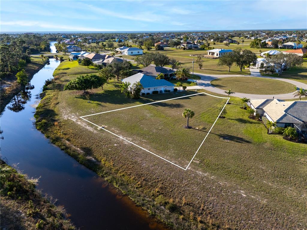 An aerial view shows a vacant, trapezoidal residential lot bordering a canal in a neighborhood — 24351 PENHOLLOW COURT, PUNTA GORDA, FL