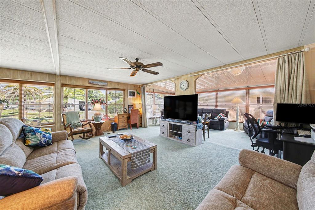 A spacious living room features wood-paneled walls, a ceiling fan, and large windows with blinds — 732 DOVE AVENUE, PORT ORANGE, FL