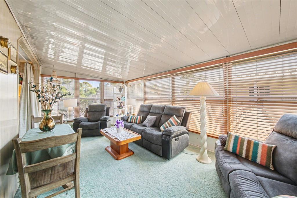 A sunroom features a light green carpet, gray sofas, a dining table, and slatted window blinds — 732 DOVE AVENUE, PORT ORANGE, FL