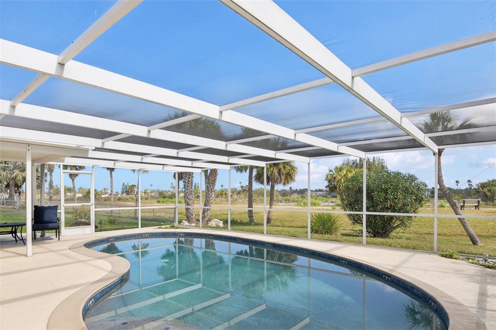 A swimming pool sits inside a screened-in lanai overlooking a grassy yard with palm trees — 3855 TOPSAIL TRAIL, NEW PORT RICHEY, FL