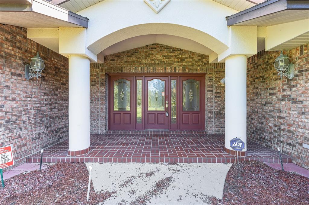 A brick house entrance features a covered porch with white columns and red double doors — 2657 W HAMPSHIRE STREET, INVERNESS, FL