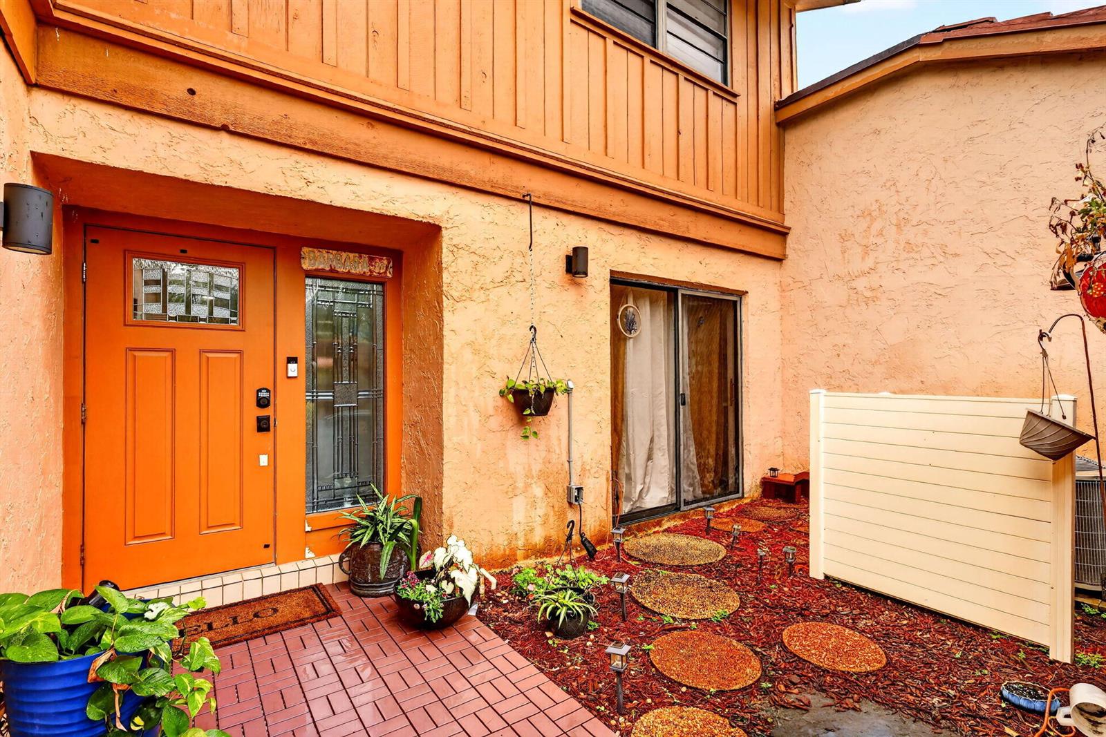An orange front door and a sliding glass door lead to a brick patio area — 5316 Stonybrook Lane, Boynton Beach FL 33437, BOYNTON BEACH, FL