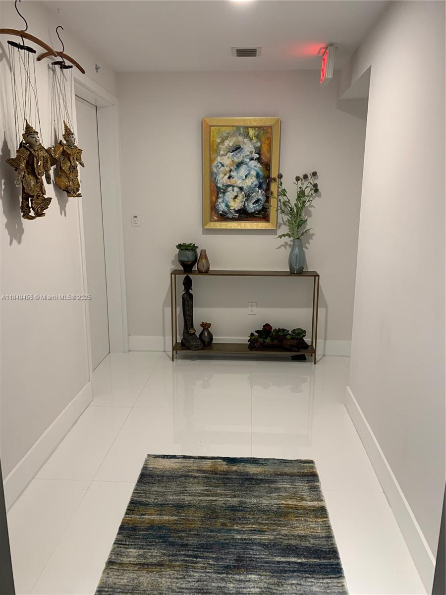 A hallway features white tile floors, a console table with decor, and wall-mounted marionettes — 16385 Biscayne Blvd, North Miami Beach FL 33160, NORTH MIAMI BEACH, FL