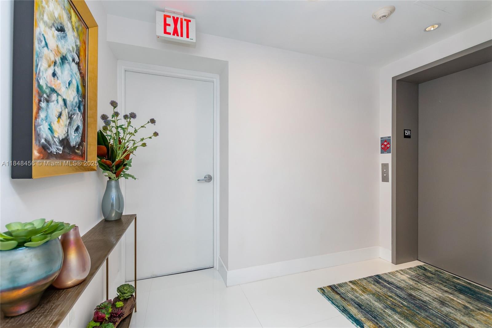 A hallway features a white door with an exit sign, an elevator, and a console table — 16385 Biscayne Blvd, North Miami Beach FL 33160, NORTH MIAMI BEACH, FL