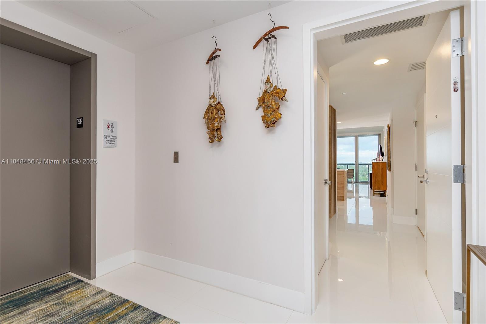 A white hallway features an elevator entrance, two hanging marionettes, and a doorway leading inside — 16385 Biscayne Blvd, North Miami Beach FL 33160, NORTH MIAMI BEACH, FL