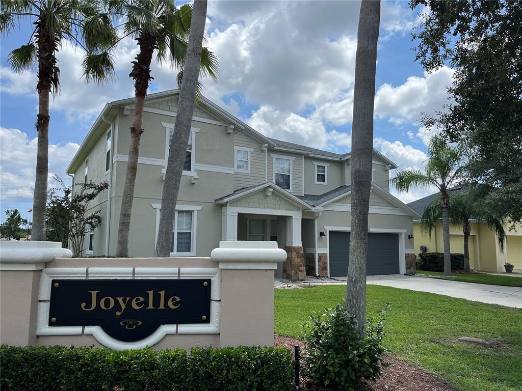 A two-story house with a beige exterior and a stone-accented entryway stands behind a sign — 101 HAGGE DRIVE, DAYTONA BEACH, FL