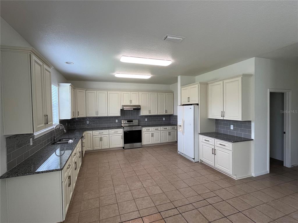 A kitchen features white cabinetry, granite countertops, gray subway tile backsplash, and tile flooring — 101 HAGGE DRIVE, DAYTONA BEACH, FL