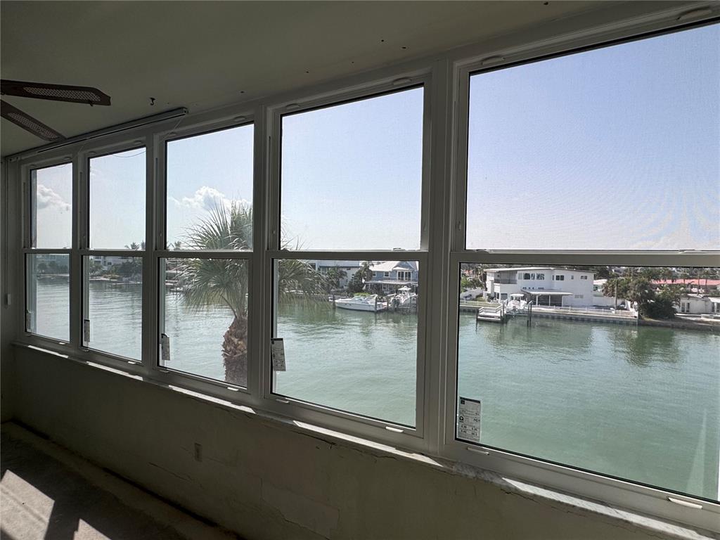 A sunroom with large windows overlooking a canal with boats and waterfront houses — 5555 GULF BOULEVARD UNIT 312, ST PETERSBURG, FL