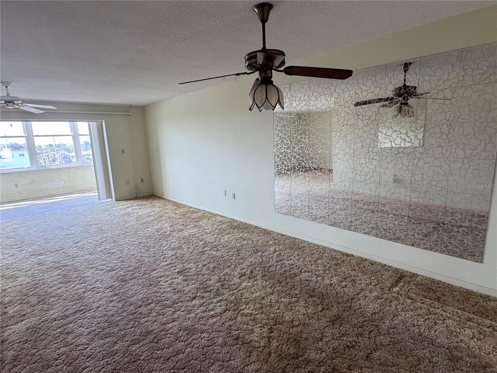 A living room features beige wall-to-wall carpeting, a ceiling fan, and a large mirrored wall — 5555 GULF BOULEVARD UNIT 312, ST PETERSBURG, FL