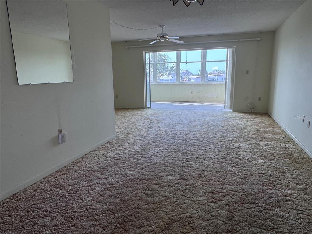 An empty living room features beige wall-to-wall carpeting, a ceiling fan, and a sliding glass door — 5555 GULF BOULEVARD UNIT 312, ST PETERSBURG, FL