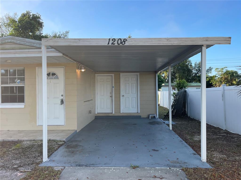 A single-story house exterior features a concrete carport, three white doors, and a white fence — 1208 CARLTON AVENUE, LAKE WALES, FL