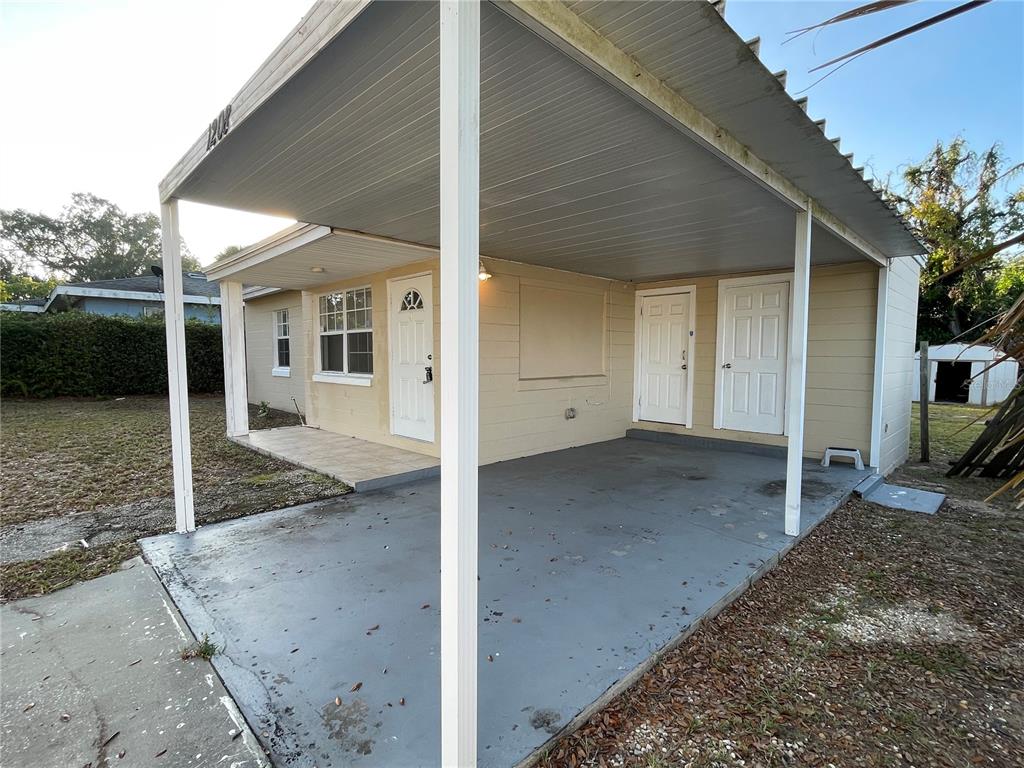 A single-story house exterior features a covered carport, a concrete driveway, and two entry doors — 1208 CARLTON AVENUE, LAKE WALES, FL
