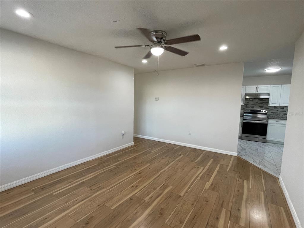 An empty room with wood-look flooring, a ceiling fan, and an adjacent tiled kitchen — 1208 CARLTON AVENUE, LAKE WALES, FL