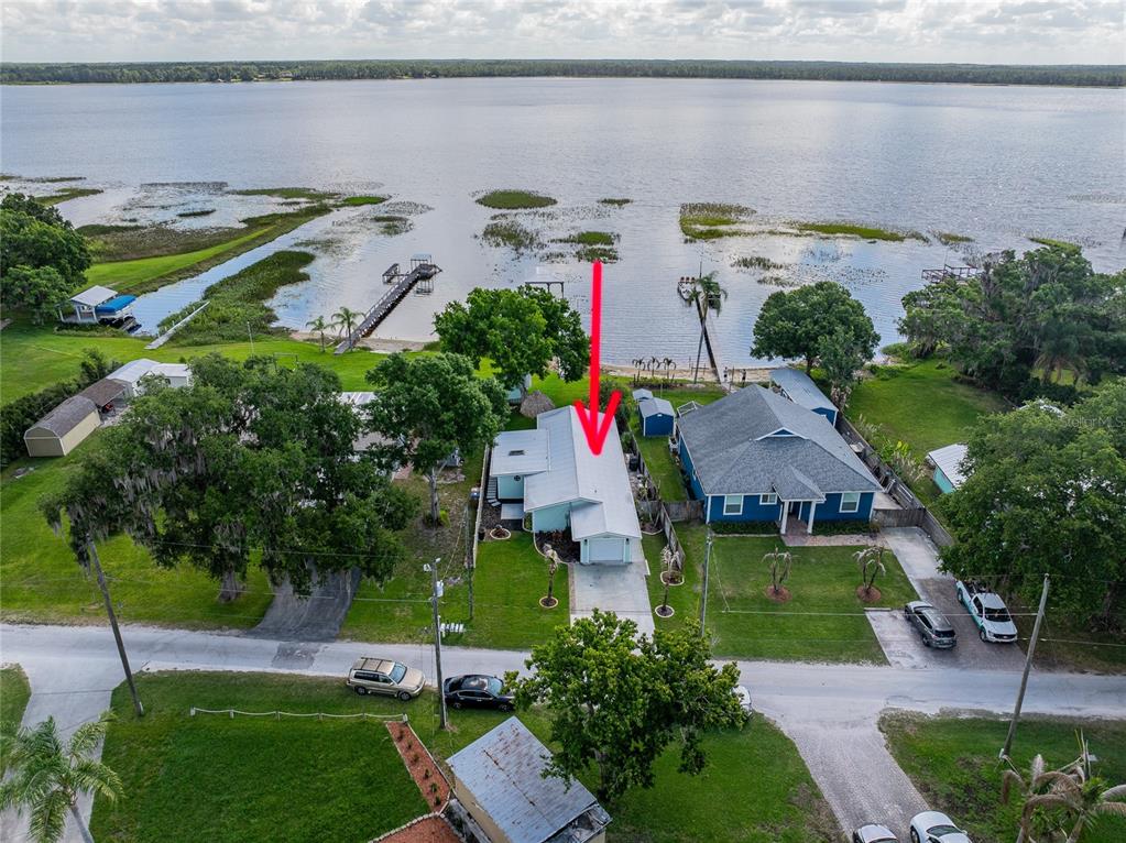 An aerial view shows a light-colored house with a metal roof near a large lake — 6125 LAKE LIZZIE DRIVE, ST CLOUD, FL