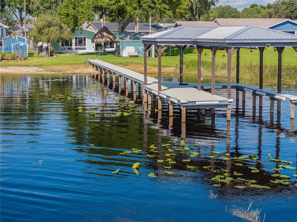A long wooden dock with a covered boat slip extends into a calm lake — 6125 LAKE LIZZIE DRIVE, ST CLOUD, FL