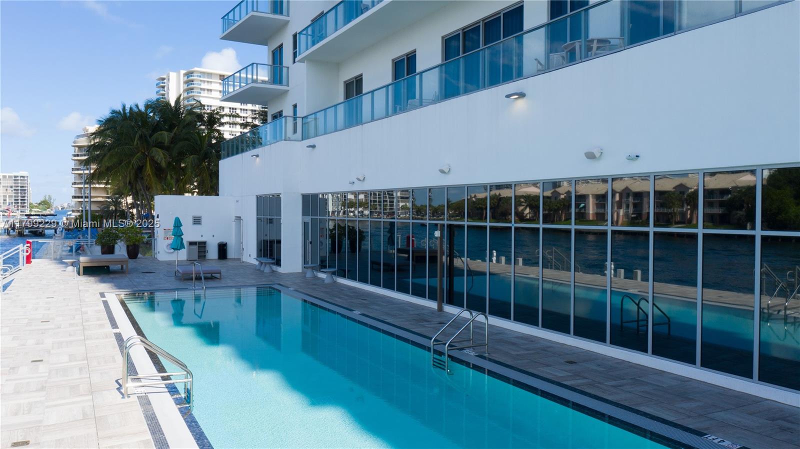 A swimming pool sits on a tiled deck beside a building with glass walls — 4010 S Ocean Dr # 1, Hollywood FL 33019, HOLLYWOOD, FL