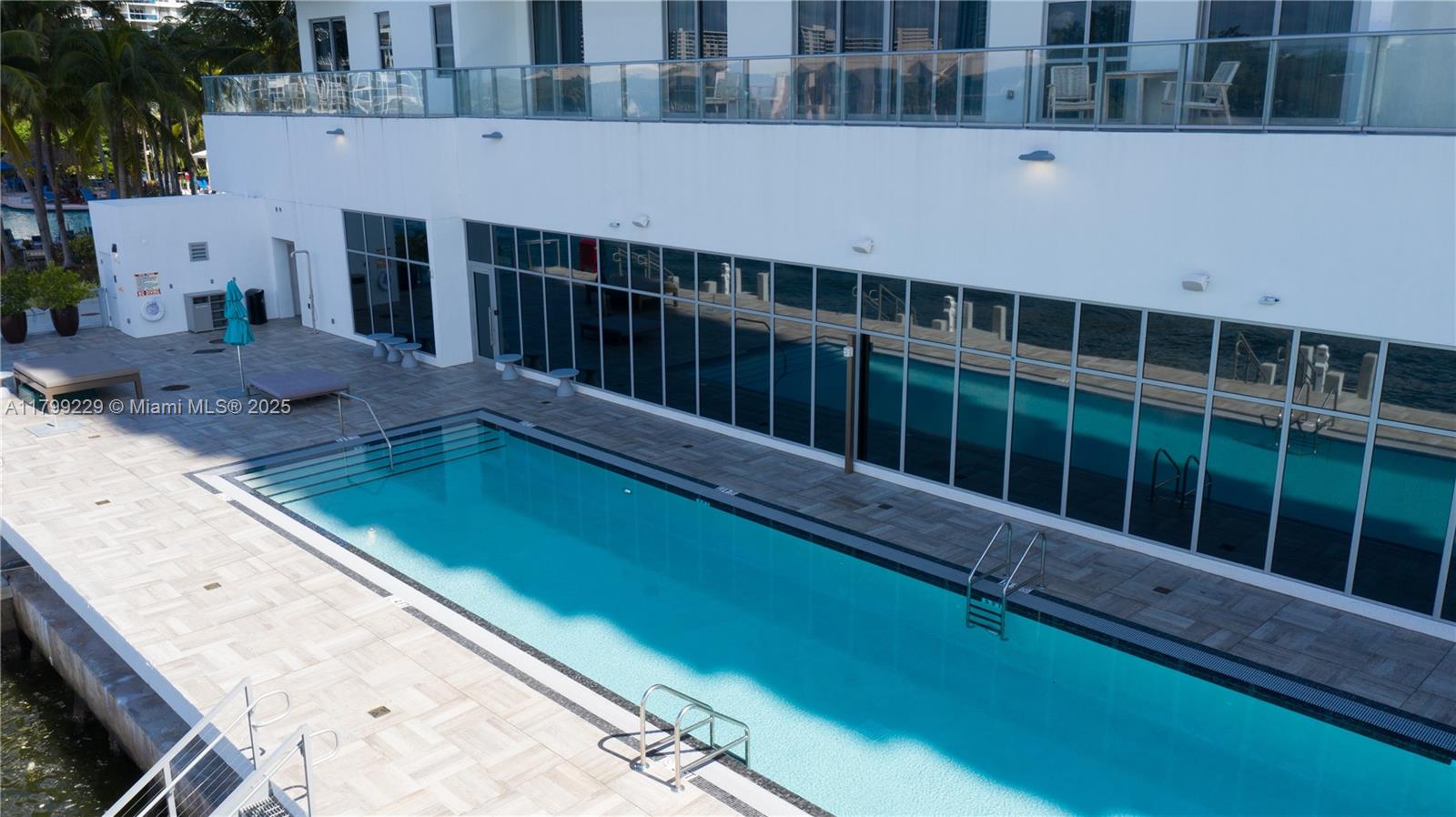 An outdoor swimming pool sits on a tiled patio next to a modern building — 4010 S Ocean Dr # 1, Hollywood FL 33019, HOLLYWOOD, FL