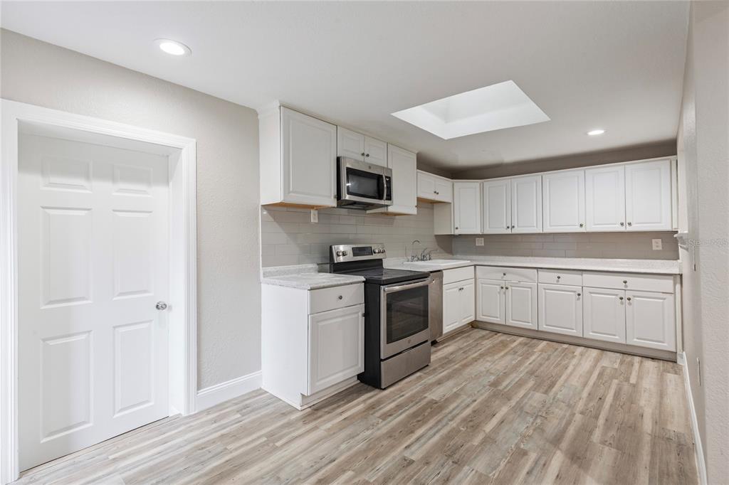 A kitchen features white cabinets, stainless steel appliances, gray tile backsplash, and light wood flooring — 1325 E LAURA STREET, PLANT CITY, FL